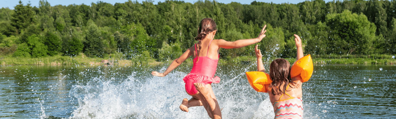 Two girls splashing happily in a lake with green trees in the background.